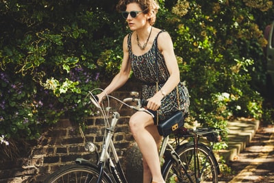 白天在绿植附近的路上骑自行车的女人